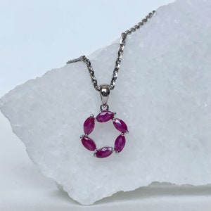 May include: A silver chain necklace with a pendant featuring a circle of pink ruby stones.