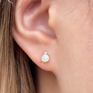 May include: A pair of silver stud earrings with a white opal gemstone and a small clear diamond accent.