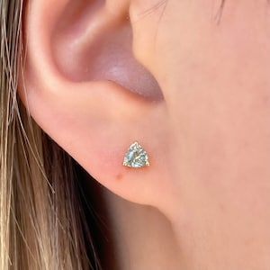 May include: A pair of gold stud earrings with a triangular shaped clear gemstone.