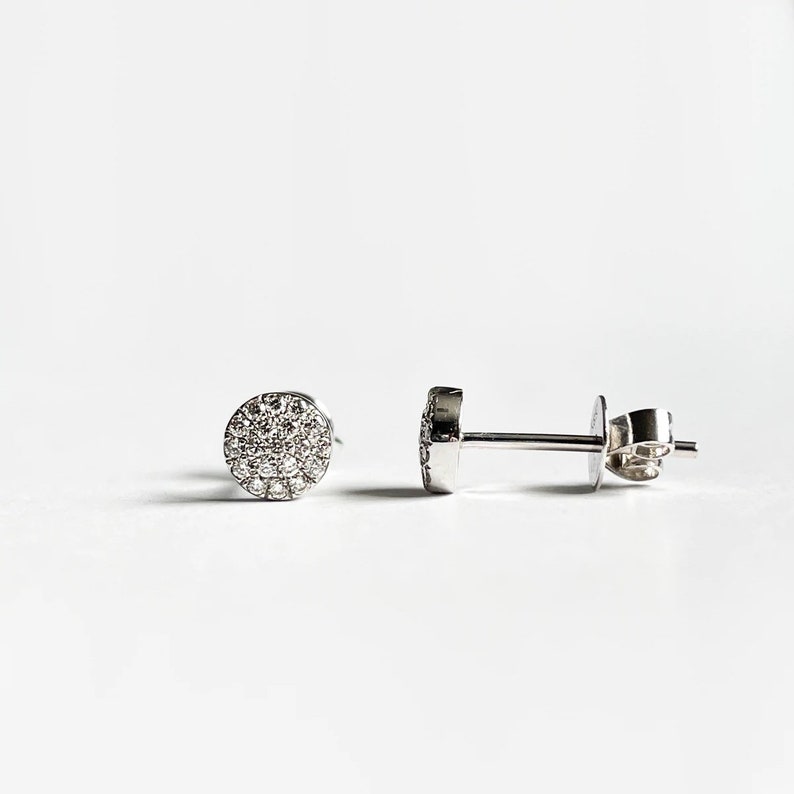 Puede incluir: Un par de pendientes de bot&oacute;n de plata con un dise&ntilde;o redondo de diamantes pav&eacute;.