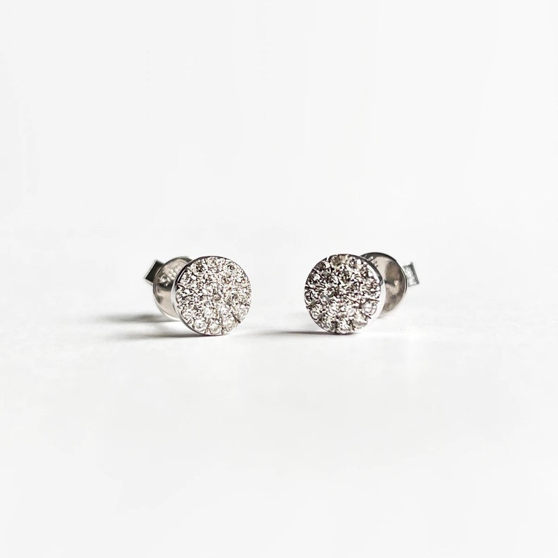Puede incluir: Un par de pendientes de bot&oacute;n de plata con un dise&ntilde;o redondo de diamantes pav&eacute;.