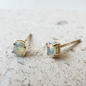 May include: A pair of gold opal stud earrings. The opals are round and have a milky white color with iridescent flashes of color.