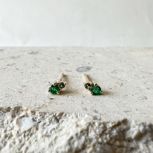 May include: A pair of gold earrings with green gemstones. The earrings are small and delicate, and they would make a great gift for someone special.
