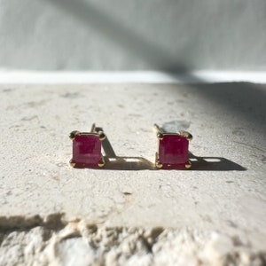 May include: A pair of gold stud earrings with square-shaped ruby gemstones.