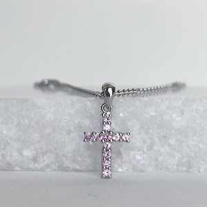 May include: A silver necklace with a small pink crystal cross pendant.