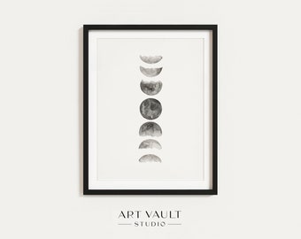May include: Black framed art print featuring a watercolor depiction of the phases of the moon. The artwork is in grayscale, with each phase of the moon rendered in varying shades of gray. The text "ART VAULT STUDIO" is printed at the bottom.