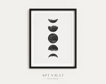 May include: Black framed art print featuring a minimalist design of the moon phases. The artwork displays the cycle of the moon in a vertical arrangement of black circles and crescents against a white background. The text "ART VAULT STUDIO" is at the bottom.