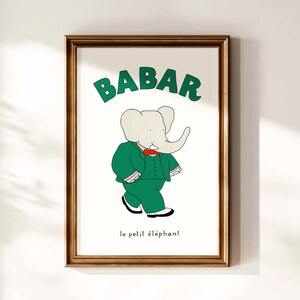 Puede incluir: Impresión enmarcada de Babar el elefante con un traje verde y pajarita roja. La palabra "BABAR" está en verde encima del elefante, con "le petit éléphant" debajo. La obra de arte está en un marco de madera marrón.