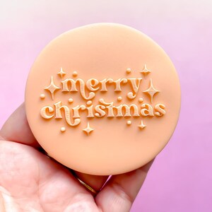 May include: A peach-coloured silicone stamp with the text "merry christmas" in a retro font, surrounded by small star shapes.