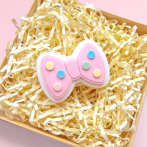 May include: A pink bow with colourful polka dots in a box filled with shredded paper.