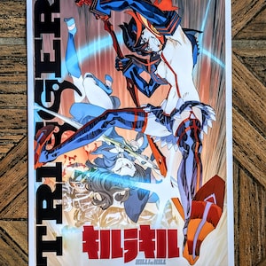 May include: A poster featuring anime-style illustrations of characters in dynamic action poses. The artwork is dominated by shades of blue, red, and orange, with Japanese text at the bottom and the word "TRIGGER" vertically on the left side.