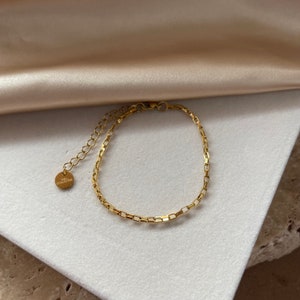 May include: A gold chain bracelet with a small round tag that says "THE COLLECTIVE".