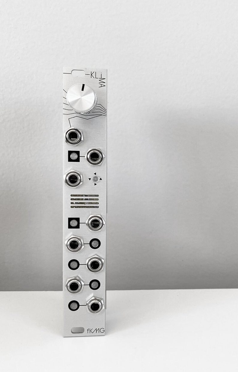 May include: A silver modular synthesizer module featuring multiple jacks, knobs, and the text "-KL/MA". The module has a series of circular and square components, and the brand name "fKMG" is printed at the bottom.