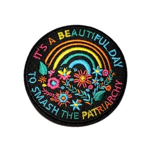 May include: Embroidered patch with a black background. The patch features a rainbow, flowers, and the text "It's a beautiful day to smash the patriarchy" in colorful thread. The patch is round.
