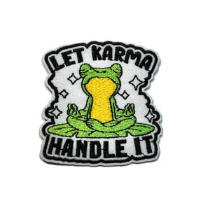 May include: Embroidered patch featuring a meditating frog in a yoga pose on a lily pad. The patch has the text "LET KARMA HANDLE IT" in black lettering. The frog is green and yellow, with a white background and black border.