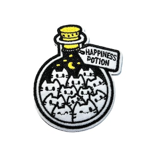 May include: Embroidered patch featuring a black potion bottle filled with white cat faces. The bottle has a yellow cork and a tag that reads "HAPPINESS POTION". The patch is outlined in black and white.