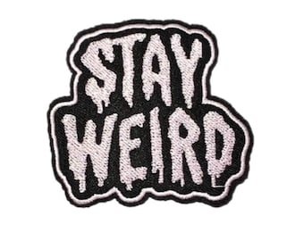 May include: Embroidered patch with the words "STAY WEIRD" in white, dripping font on a black background. The patch has a white border and is likely for clothing or accessories.