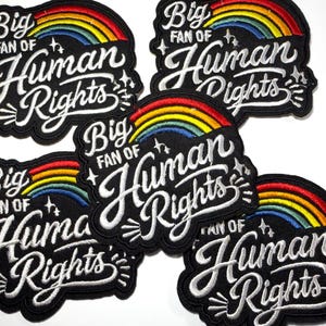 May include: Five black embroidered patches featuring a colorful rainbow arch above the white stitched text "Big FAN OF Human Rights" with small star accents. Each patch has a scalloped border and a black background with white lettering.