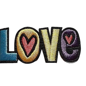 May include: Embroidered patch spelling out the word "LOVE" in colorful, bubble letters. The letters are outlined in black, with a heart design in the center of the "O" and "E". The patch is on a white background.