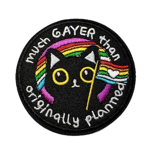 May include: A round, black embroidered patch featuring a black cat with yellow eyes and a rainbow flag. The text "much gayer than originally planned" is embroidered around the cat in white.