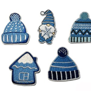 May include: Five embroidered patches in shades of blue and white. The patches include two winter hats, a gnome holding a snowflake, and a house. The patches are outlined in white.