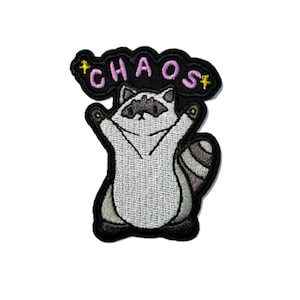 May include: Embroidered patch featuring a cartoon raccoon with its arms raised. The raccoon is primarily gray and white with black accents. Above the raccoon is the word "CHAOS" in pink letters with yellow stars. The patch has a black border.
