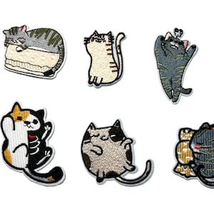 May include: Set of six embroidered cat patches in various poses. Includes a sleeping cat on a stack, a standing cat, a cat reaching up, a cat with a skeleton design, a cat curled up, and a cat wrapped in a mummy design.