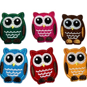 May include: Six colorful owl patches in green, pink, brown, blue, red, and orange. Each patch features large black eyes, a yellow beak, and brown accents. The patches are embroidered with a detailed design, perfect for adding to clothing or accessories.