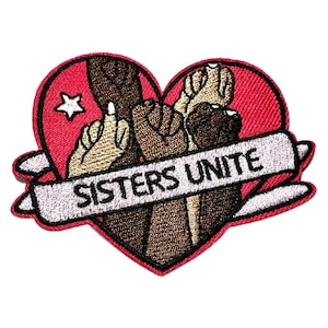 May include: Embroidered patch featuring a red heart with a white star and the words "SISTERS UNITE" on a banner. The heart design includes hands with different skin tones, symbolizing unity and solidarity.