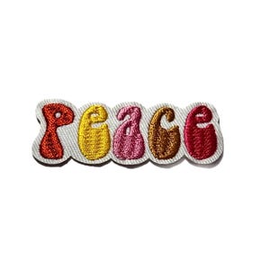 May include: Embroidered patch with the word "peace" in a retro font. The letters are in shades of red, yellow, pink, and brown, outlined in a darker color, and set against a white background.