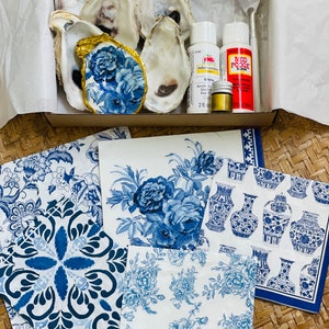 May include: A craft kit for making decorative oyster shell dishes. The kit includes oyster shells, blue and white patterned decoupage paper, Mod Podge glue, white acrylic paint, and a small gold paint bottle.