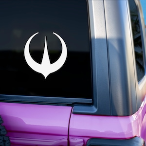 Pode incluir: Um adesivo de vinil branco com a forma de uma seta estilizada sobre um fundo preto. O adesivo é aplicado na janela traseira de um Jeep rosa.