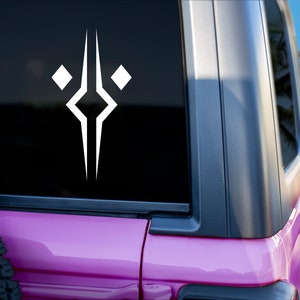 May include: A white vinyl decal featuring a symmetrical geometric design with a central vertical line, a diamond shape in the middle, and two smaller diamond shapes on either side, applied to the rear window of a pink vehicle.