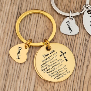 May include: Two keychains with round and heart-shaped pendants. One keychain is gold-toned with the name "Daniel" on a heart pendant. The other is silver-toned with "Vivian" on a heart pendant. Both have a round pendant with an engraved cross and text.