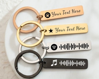 Könnte beinhalten: Vier personalisierte Schlüsselanhänger mit Metallringen. Ein roségoldener Schlüsselanhänger hat einen Pfotenabdruck und den Text "Your Text Here". Ein goldener Schlüsselanhänger hat einen Stern und den Text "Your Text Here". Ein silberner Schlüsselanhänger hat einen Spotify-Code. Ein schwarzer Schlüsselanhänger hat eine Musiknote und eine Schallwelle.