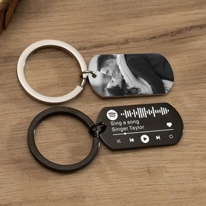 Op de afbeelding: Zwarte metalen sleutelhanger met een foto van een stel en een Spotify-code met de tekst "Sing a song Singer Taylor".