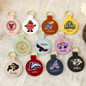 Puede incluir: Una colección de llaveros redondos en varios colores, cada uno con un logotipo o diseño diferente. Los llaveros tienen anillos dorados y están dispuestos sobre una superficie clara. Algunos llaveros tienen nombres.