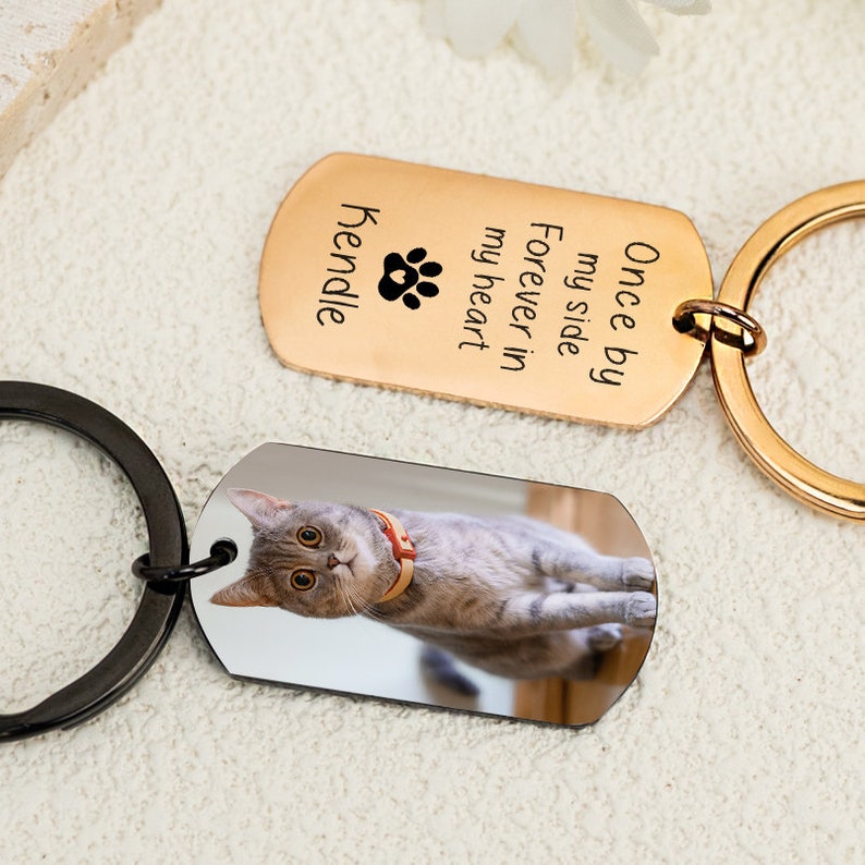 May include: Gold and black keychain with a photo of a cat on one side and the text "Once by my side forever in my heart Kendall" on the other side.