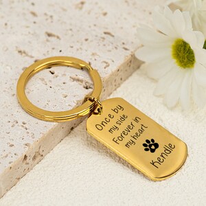 May include: Gold-tone keychain with a dog paw print and the text "Once by my side Forever in my heart Kendale".