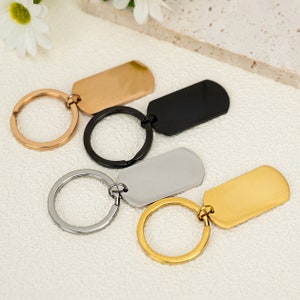 May include: Four keychains with different coloured metal tags. The tags are rectangular and have a smooth, polished finish. The keychains are silver, gold, rose gold, and black.
