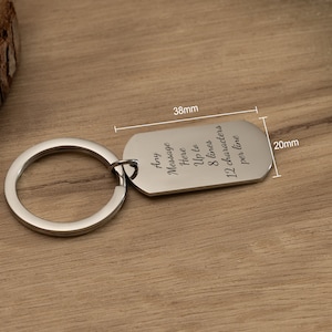 May include: Silver keychain with a rectangular tag that reads "Any Message Here Up to 8 lines 12 characters per line". The tag is 3.8 cm long and 2 cm wide.