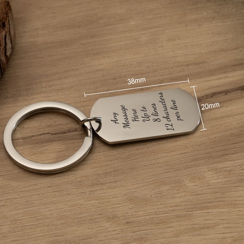 May include: Silver keychain with a rectangular tag that reads "Any Message Here Up to 8 lines 12 characters per line". The tag is 3.8 cm long and 2 cm wide.
