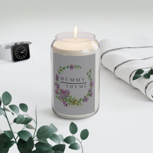 May include: A clear glass candle jar with a grey label. The label has a wreath of thyme flowers and the text "MUMMY THYME".