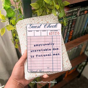 May include: A pink and white guest check with the text "Guest Check" at the top. The check number is 603155. The text "emotionally unavailable due to fictional men" is written in blue ink on the check. The check has a "Thank You" message at the bottom.