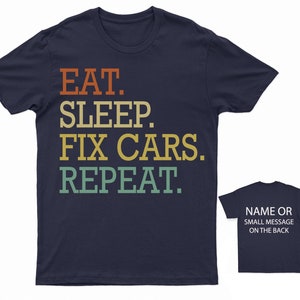 Puede incluir: Camiseta azul marino con el texto "EAT. SLEEP. FIX CARS. REPEAT." en un esquema de color retro. La parte posterior de la camiseta tiene espacio para un nombre o un mensaje peque&ntilde;o.