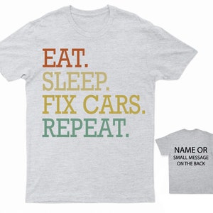Puede incluir: Una camiseta gris jaspeada con el texto "EAT. SLEEP. FIX CARS. REPEAT." impreso en un esquema de color retro. La parte posterior de la camiseta tiene espacio para un nombre o un mensaje peque&ntilde;o.