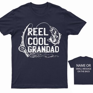 May include: Navy blue t-shirt with a white graphic of a fishing rod and a fish. The text "REEL COOL GRANDAD" is printed on the shirt.