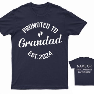 May include: Navy blue t-shirt with white text that reads "Promoted to Grandad Est. 2024" with a pair of white footprints above the word "Grandad".