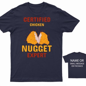 Op de afbeelding: Donkerblauw T-shirt met een afbeelding van een kippenkroket en de tekst "Certified Chicken Nugget Expert".