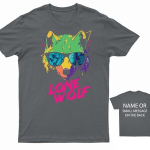 May include: A dark gray t-shirt with a colorful graphic of a wolf wearing sunglasses. The text "LONE WOLF" is printed in pink below the wolf.